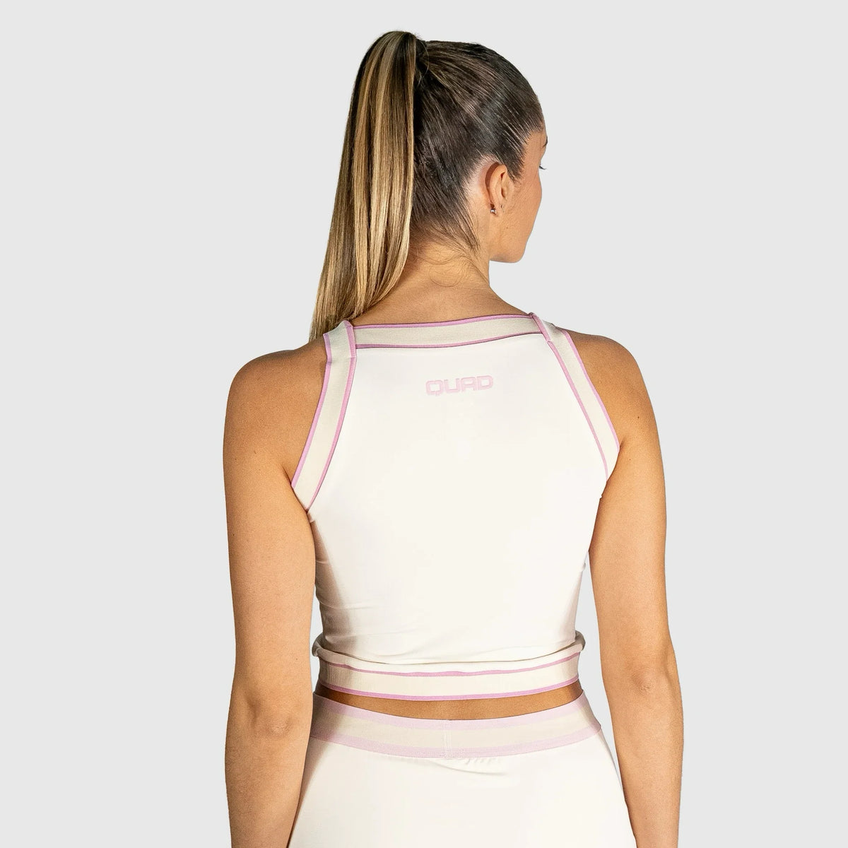 Woman wearing a slice padel top with pink accents on a plain background